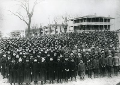 Black and white photo of school children in uniforms, black dresses on the girls and military style jackets and pants on the boys