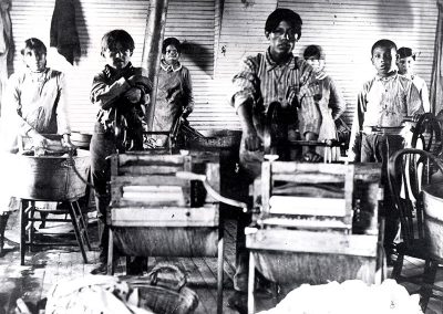 1901 black and white photo of young Native boys in a laundry room in front of wringing machines and wash tubs