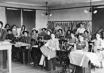1900 black and white photograph of classroom with Native young women at sewing machines