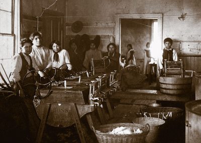 1890 black and white photo of Native youth in laundry room with manual equipment for doing laundryunderneath