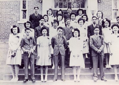 1940 black and white photo of young Native men and women dresses and suits posing on steps leading up to a brick building.