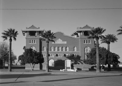 Black and white photo of a 3 story brick building with a mission-style facade and towers on both front corners.