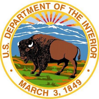 US Dept of Interior seal showing a buffalo standing on open grassland and earth in front of blue silhouetted mountains with the sun rising in the background. The words US Department of Interior, March 3, 1849 ring the image.